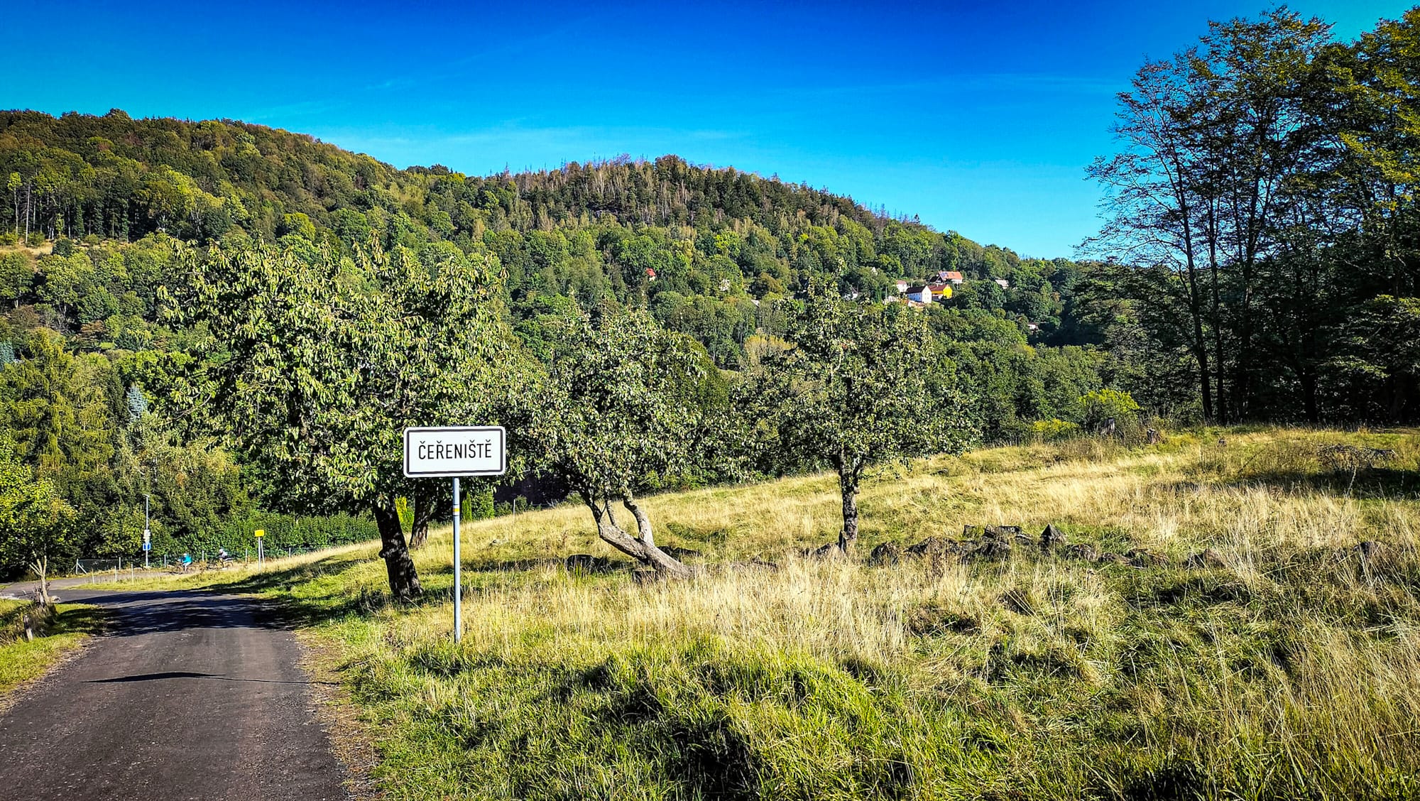 Eine schmale Straße mit dem Ortsschild von Čeřeniště in Böhmen.