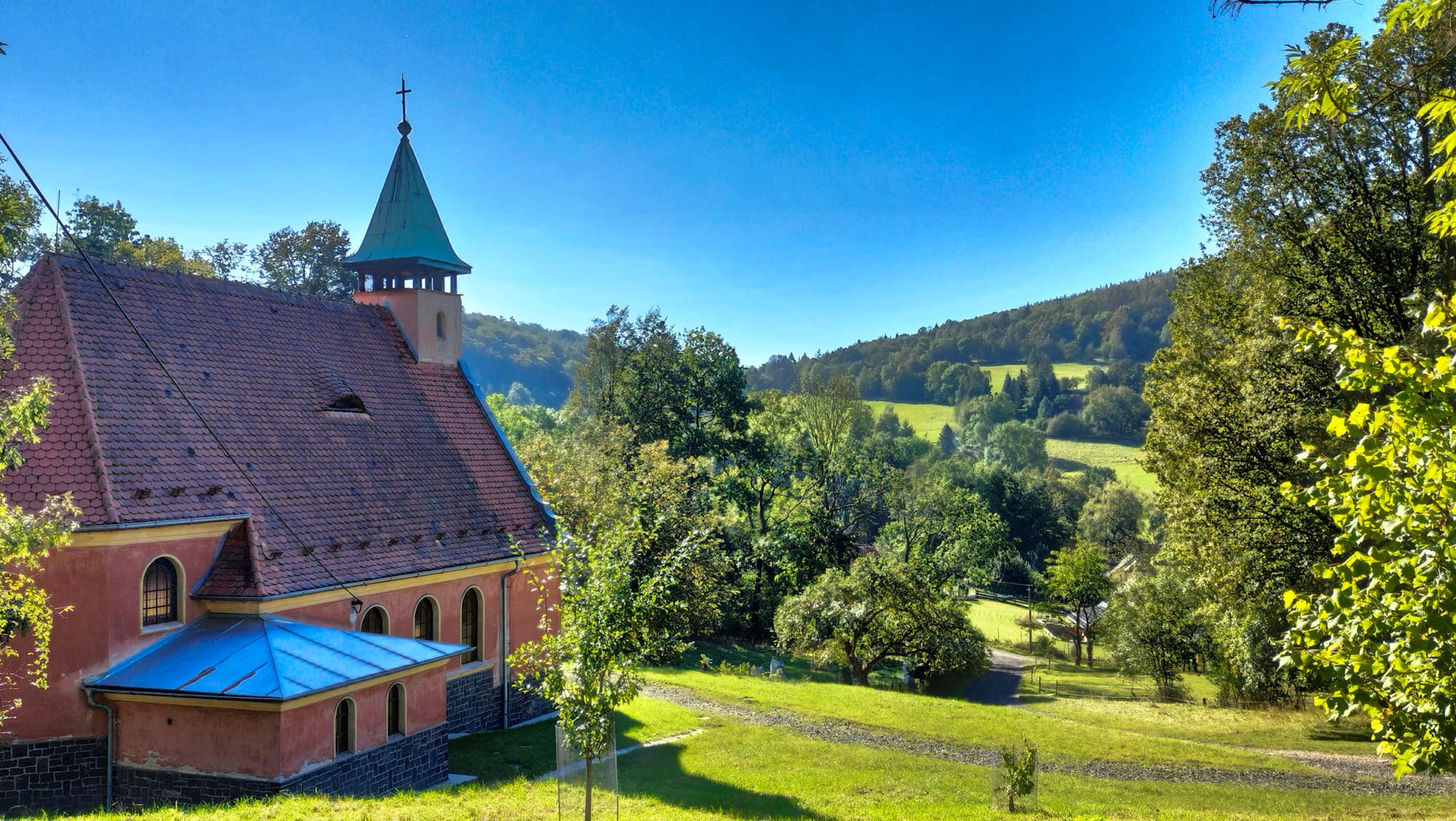 Eine kleine rosafarbene Dorfkirche an einem Hügel in Čeřeniště in Böhmen.