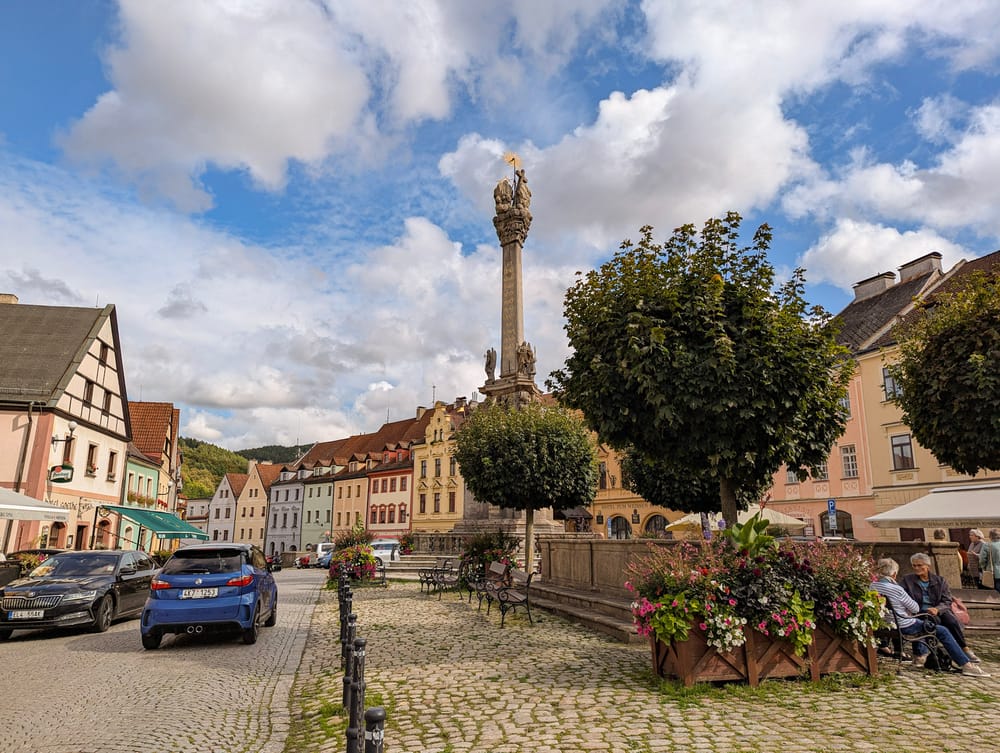 Ein Marktplatz einer tschechischen Kleinstadt mit Mariensäule, Brunnen und Blumenrabatten.